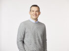 Man standing, smiling, in a light gray crewneck sweater.