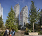 Photograph of Thames City Phase One, two tall residential towers with surrounding trees and greenery. Three people are pictured as they walk towards the development.